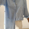 Chemise bleu clair à col classique ornée de strass, portée avec un pantalon écru.