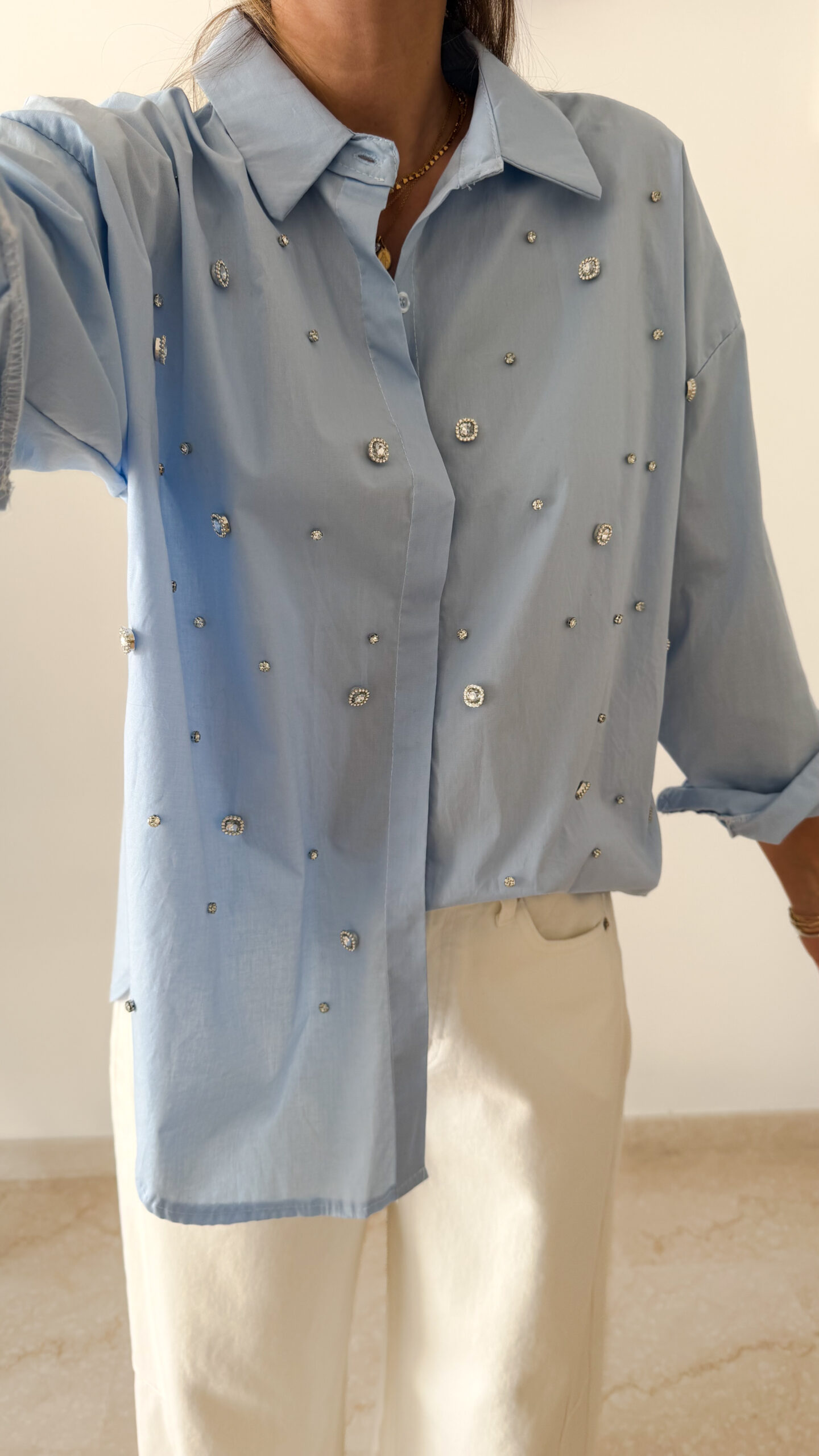 Chemise bleu clair à col classique ornée de strass, portée avec un pantalon écru.