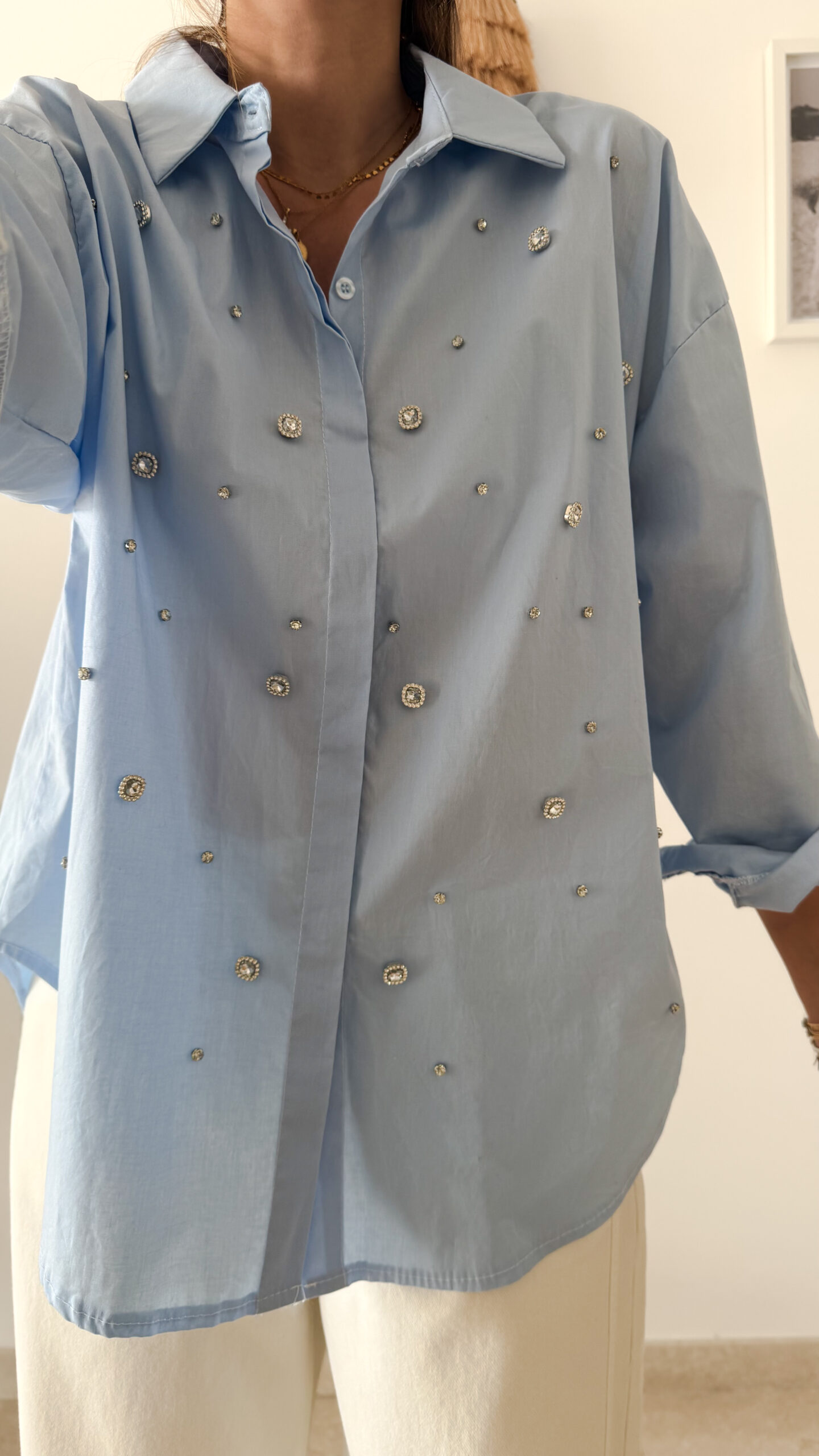 Chemise bleu clair à col classique ornée de strass, portée avec un pantalon écru.