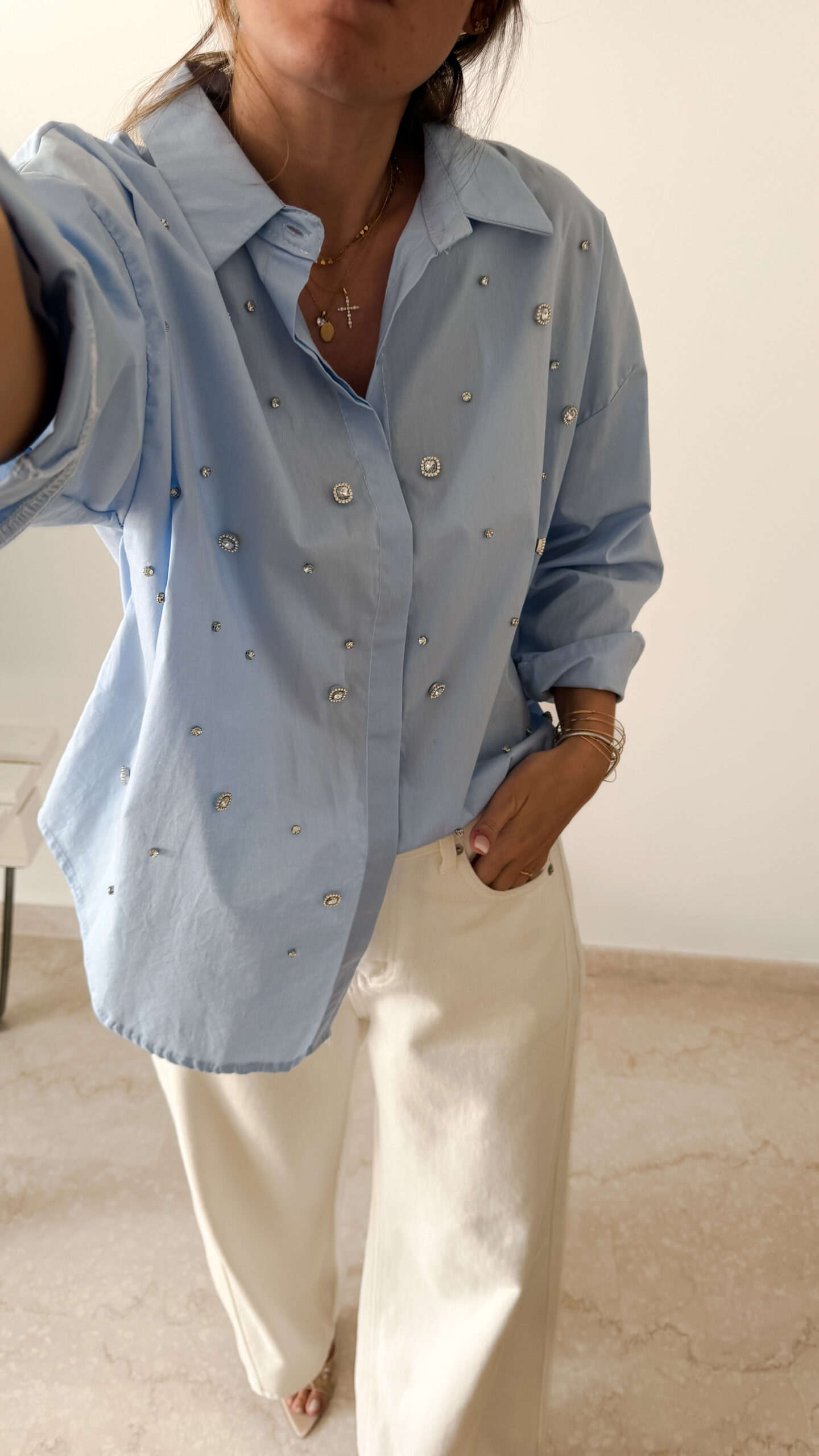 Chemise bleu clair à col classique ornée de strass, portée avec un pantalon écru.