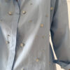 Chemise bleu clair à col classique ornée de strass, portée avec un pantalon écru.