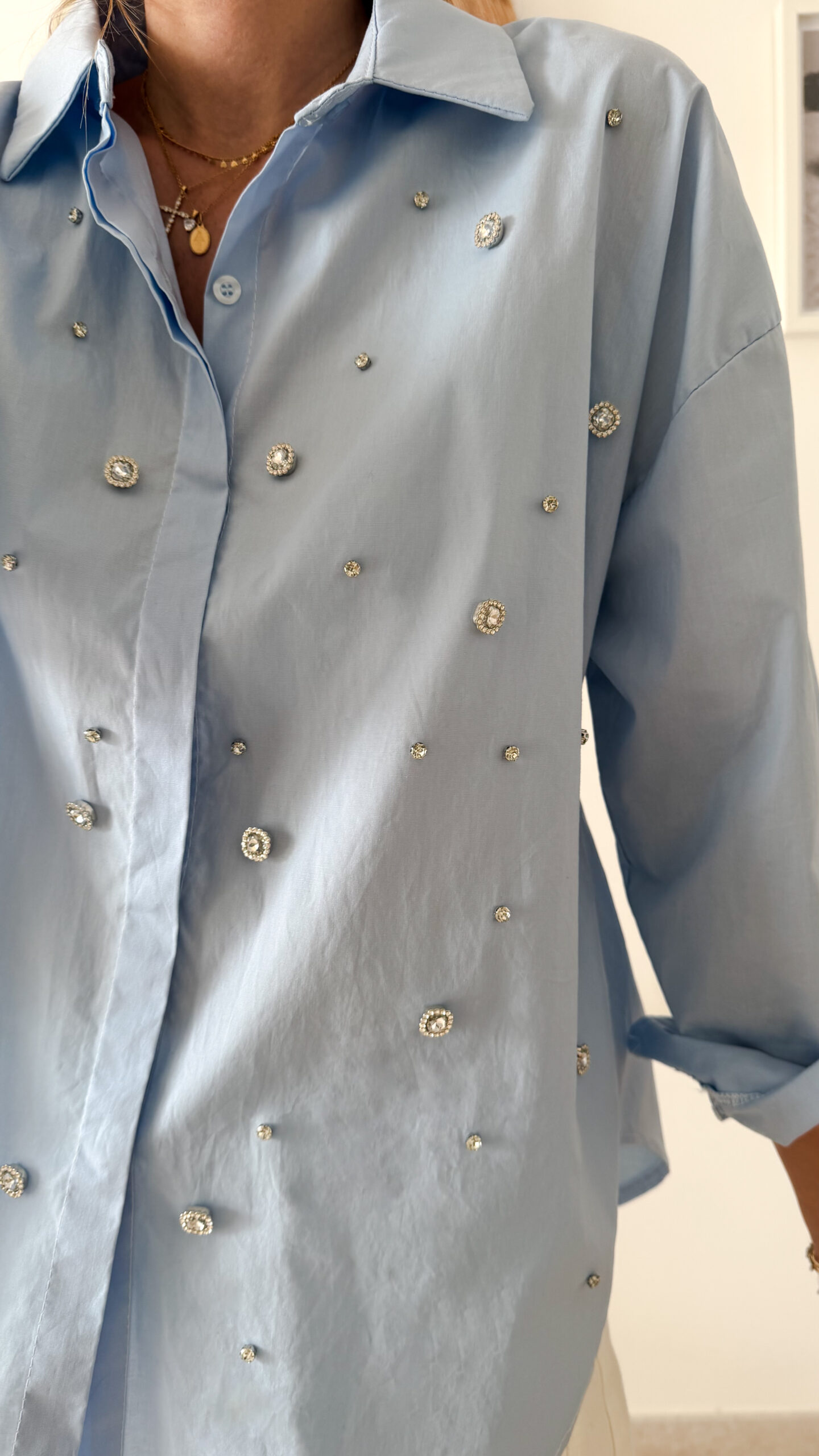 Chemise bleu clair à col classique ornée de strass, portée avec un pantalon écru.