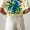 T-shirt jaune pâle avec imprimé tropical bleu et vert porté avec un jean blanc taille haute.