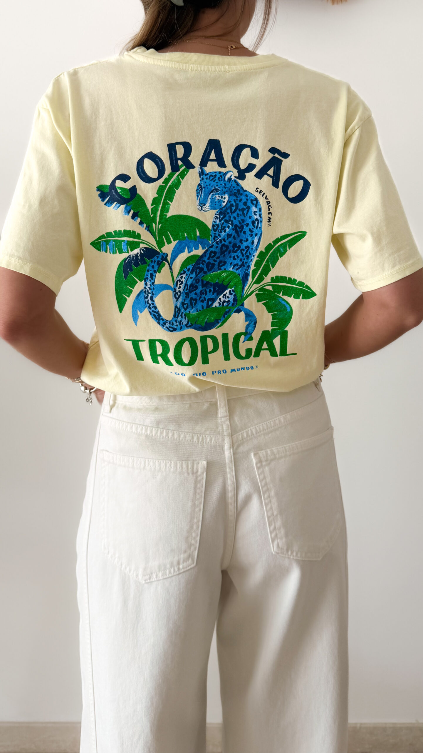 T-shirt jaune pâle avec imprimé tropical bleu et vert porté avec un jean blanc taille haute.
