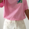 T-shirt rose avec imprimé tropical bleu et vert porté avec un jean blanc taille haute.