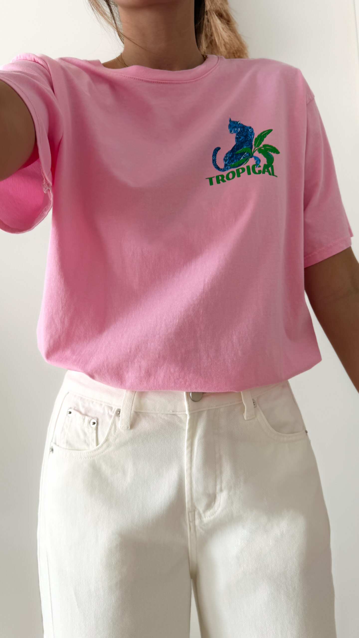 T-shirt rose avec imprimé tropical bleu et vert porté avec un jean blanc taille haute.