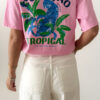 T-shirt rose avec imprimé tropical bleu et vert porté avec un jean blanc taille haute.