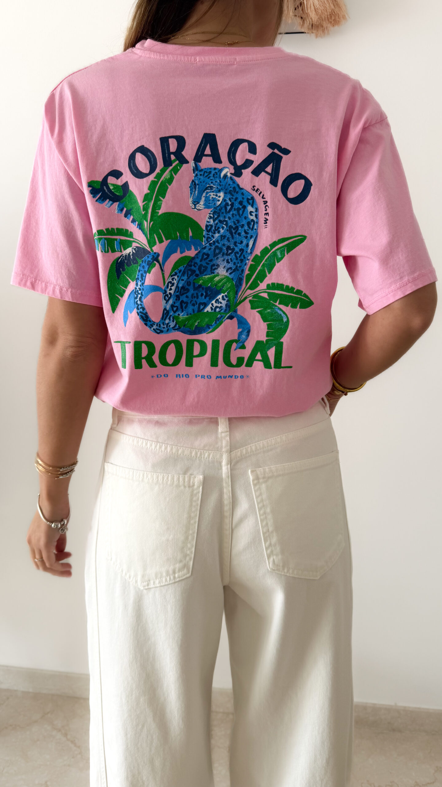 T-shirt rose avec imprimé tropical bleu et vert porté avec un jean blanc taille haute.
