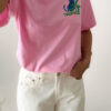 T-shirt rose avec imprimé tropical bleu et vert porté avec un jean blanc taille haute.