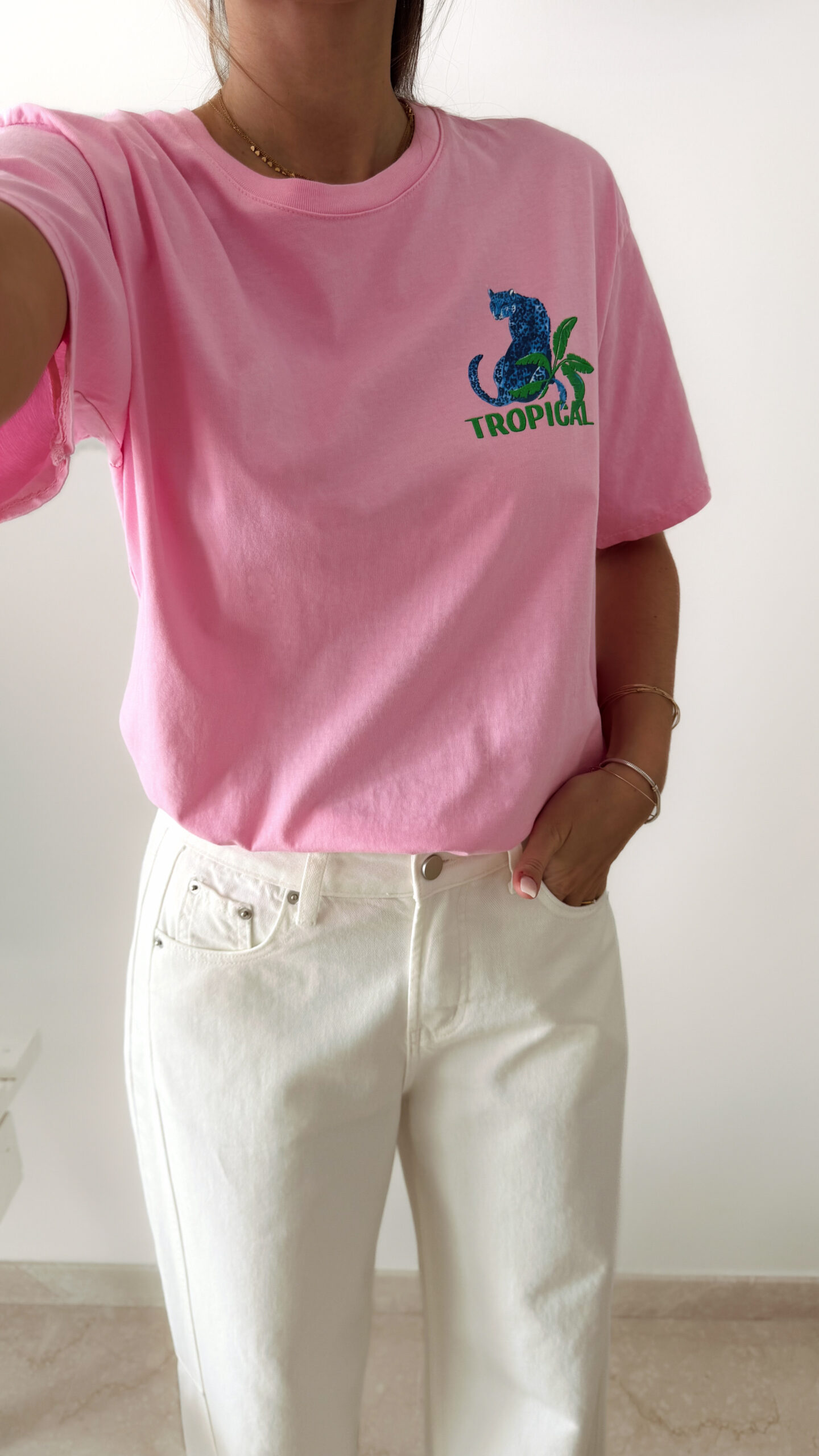 T-shirt rose avec imprimé tropical bleu et vert porté avec un jean blanc taille haute.
