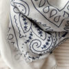 Foulard blanc à motif cachemire noir porté avec un pull crème et un pantalon blanc.