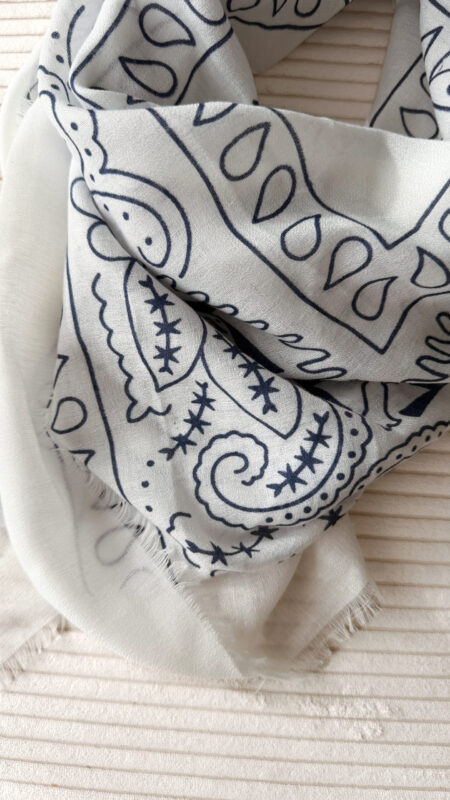 Foulard blanc à motif cachemire noir porté avec un pull crème et un pantalon blanc.