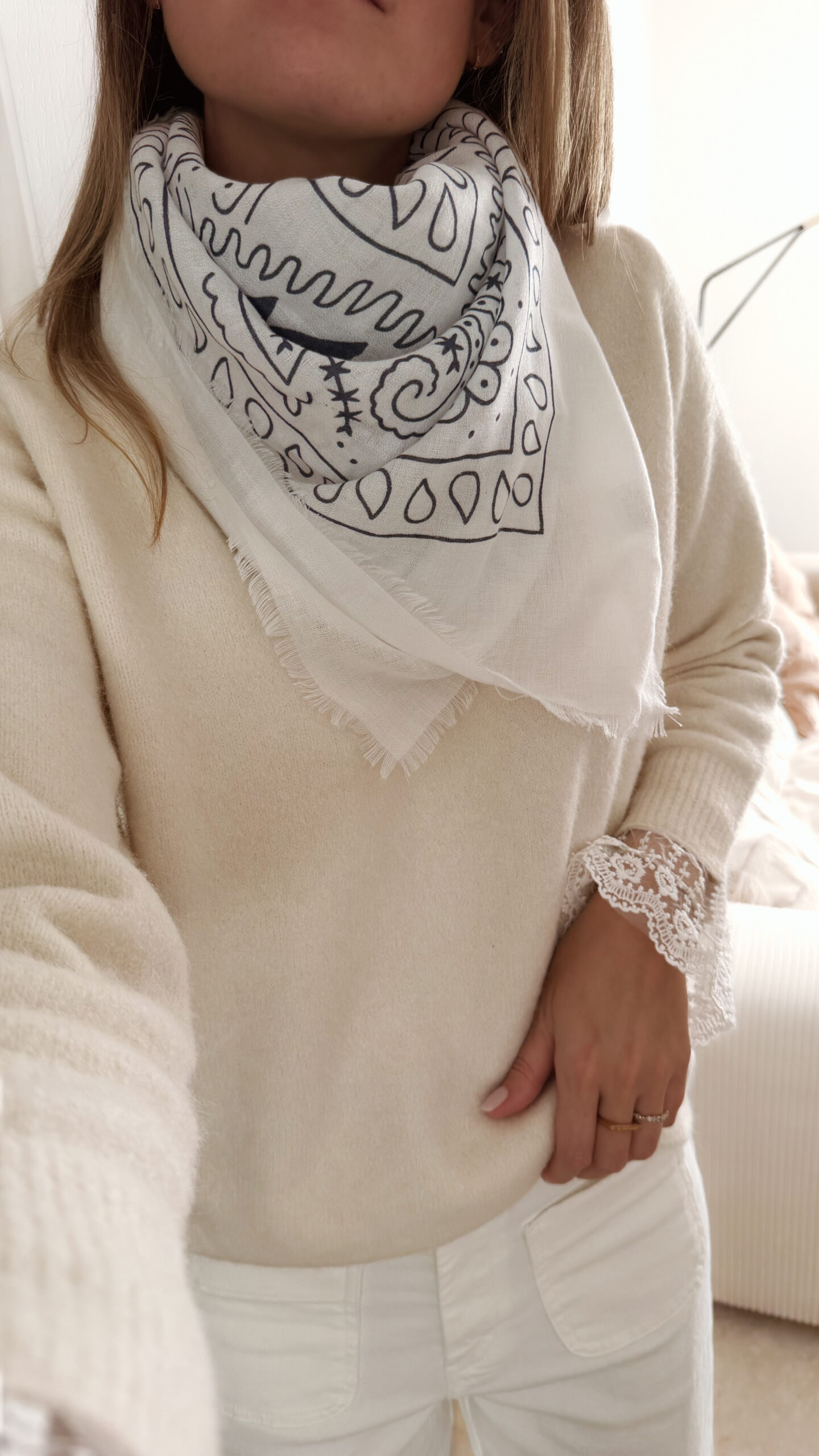 Foulard blanc à motif cachemire noir porté avec un pull crème et un pantalon blanc.