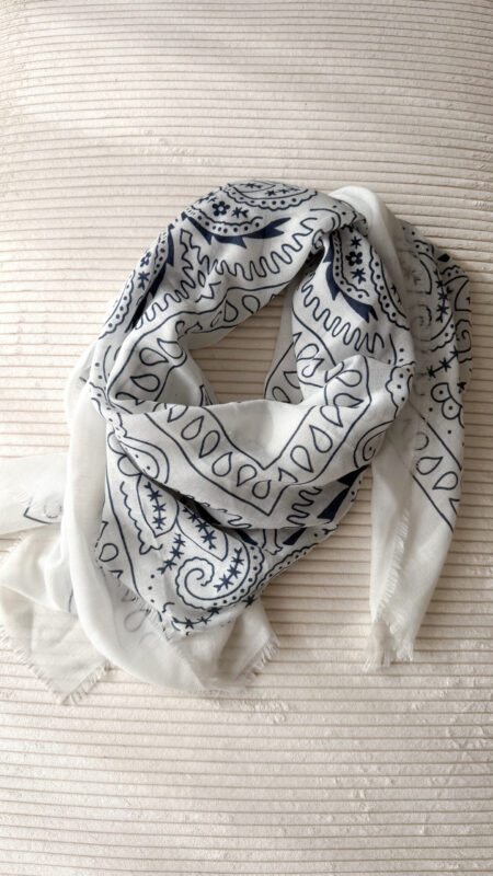 Foulard blanc à motif cachemire noir porté avec un pull crème et un pantalon blanc.