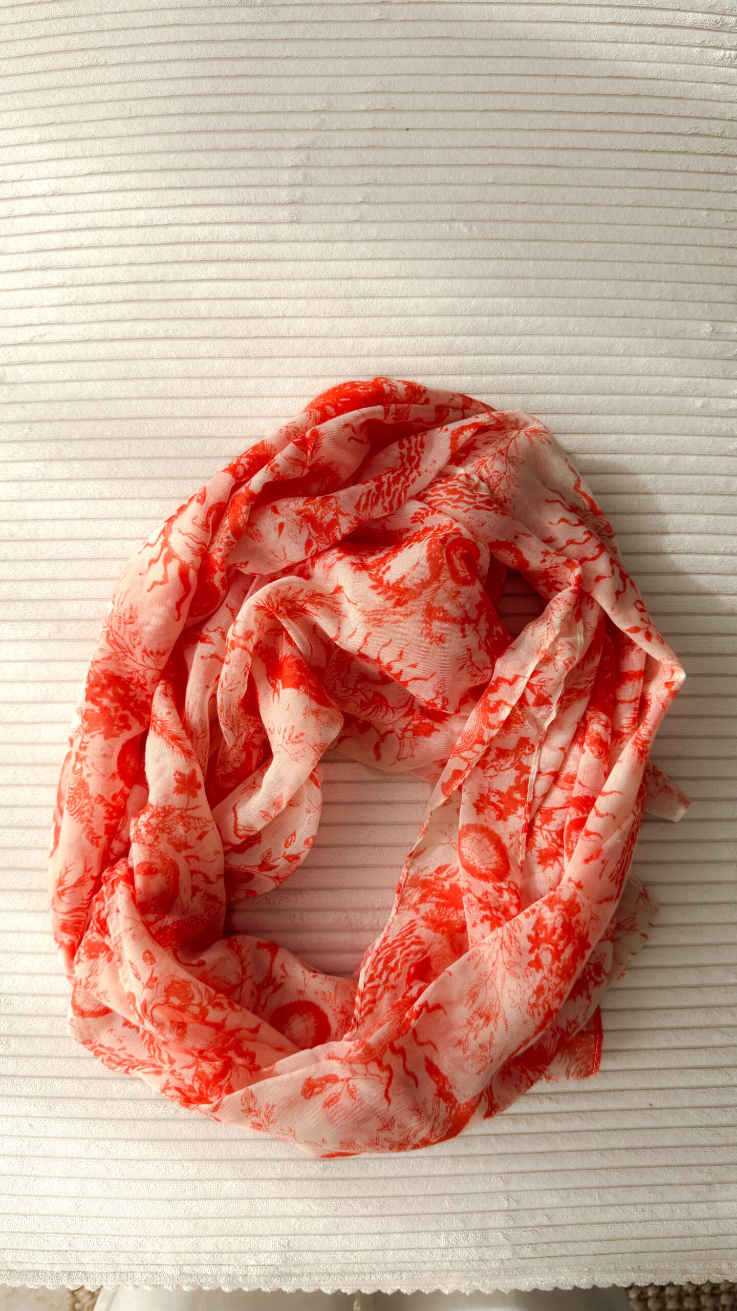 Foulard rose et orange motif Toile de Jouy porté avec pull beige et pantalon blanc
