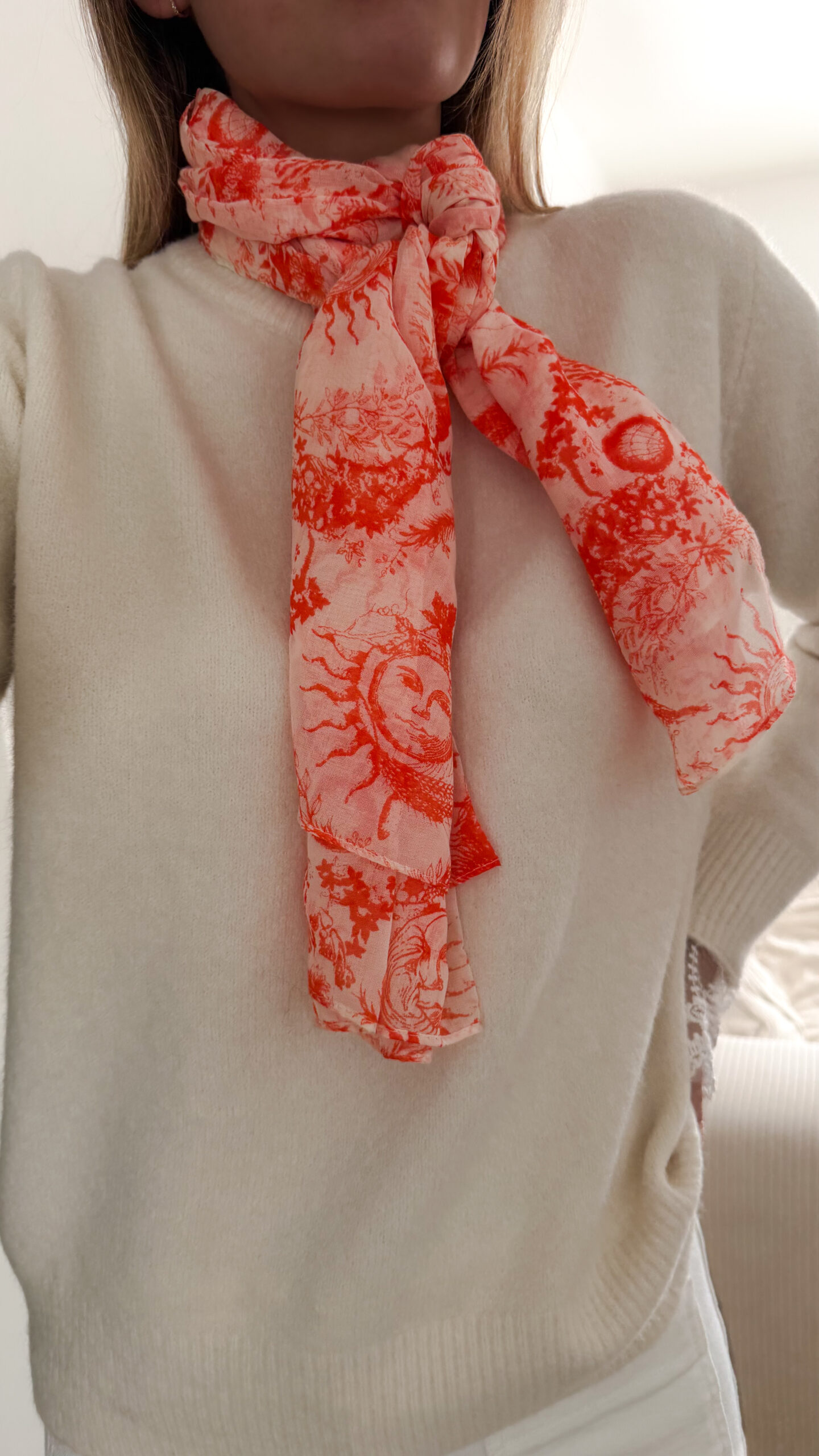 Foulard rose et orange motif Toile de Jouy porté avec pull beige et pantalon blanc