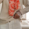 Foulard rose et orange motif Toile de Jouy porté avec pull beige et pantalon blanc