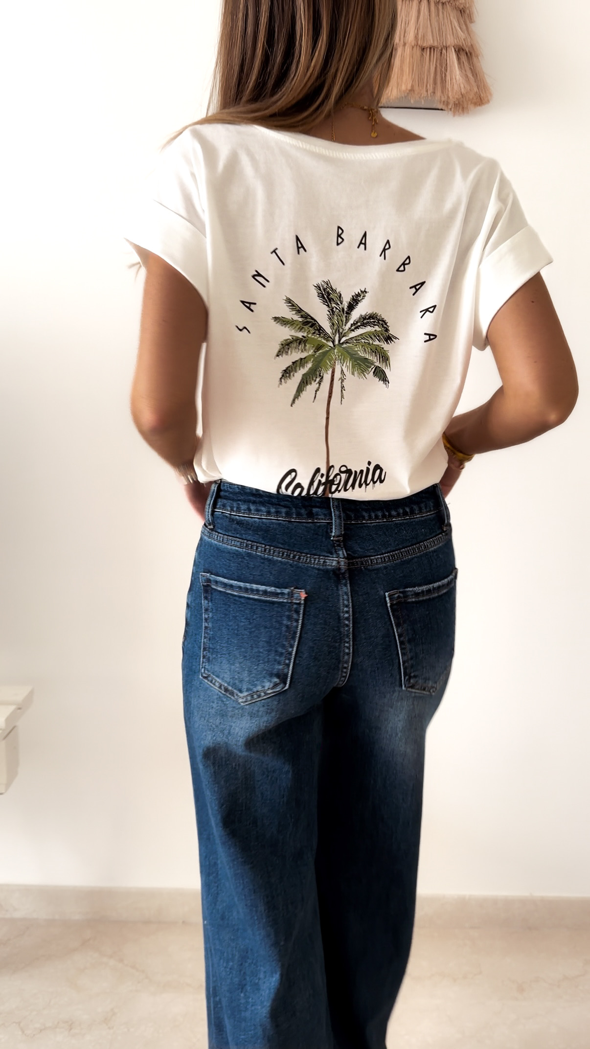 T-shirt blanc à manches retroussées avec imprimé palmier « Santa Barbara California » au dos, porté avec un jean large taille haute.