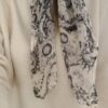 Foulard blanc et noir à imprimé artistique porté autour du cou avec un pull écru.