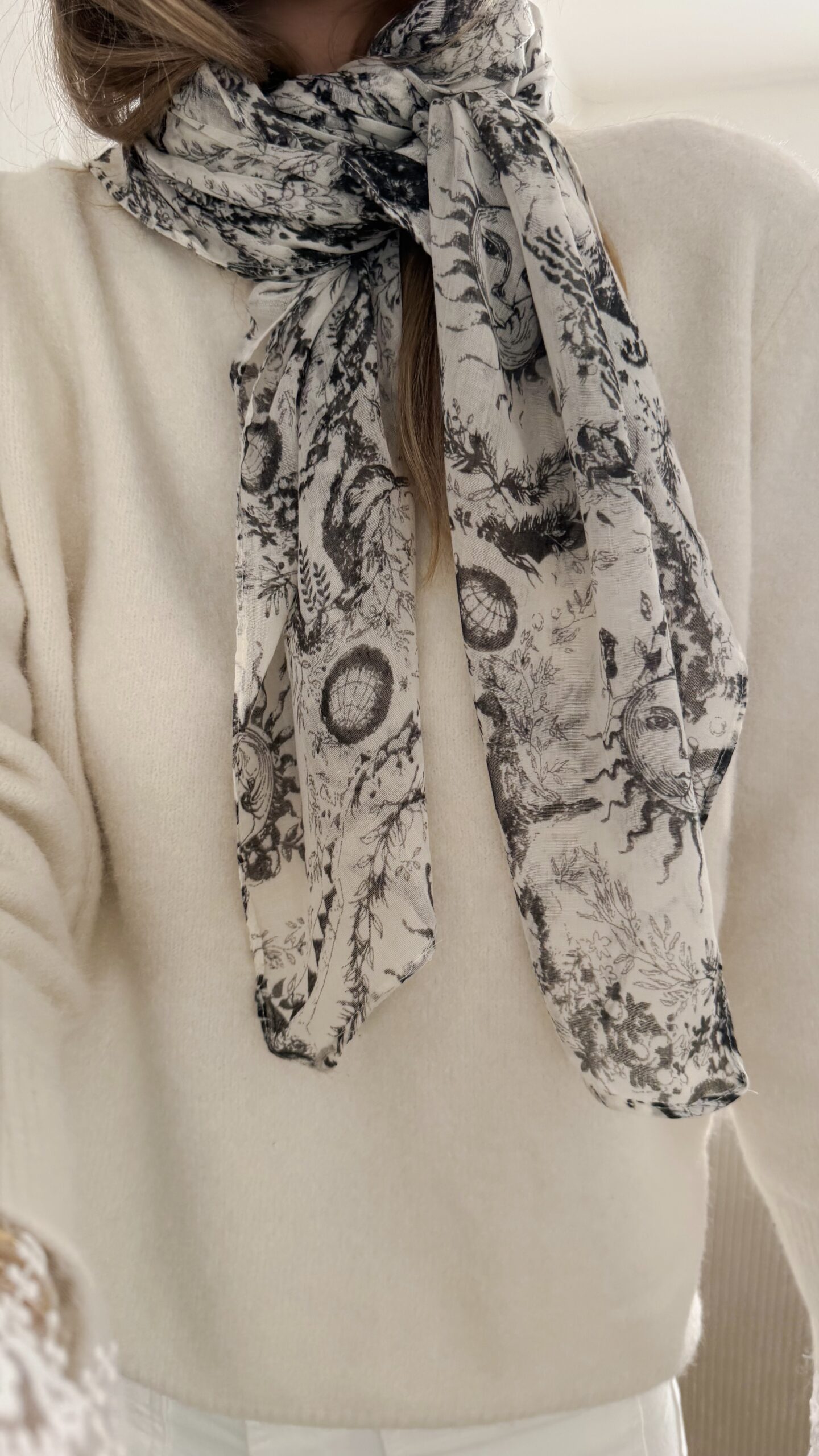 Foulard blanc et noir à imprimé artistique porté autour du cou avec un pull écru.