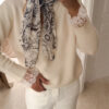 Foulard blanc et noir à imprimé artistique porté autour du cou avec un pull écru.