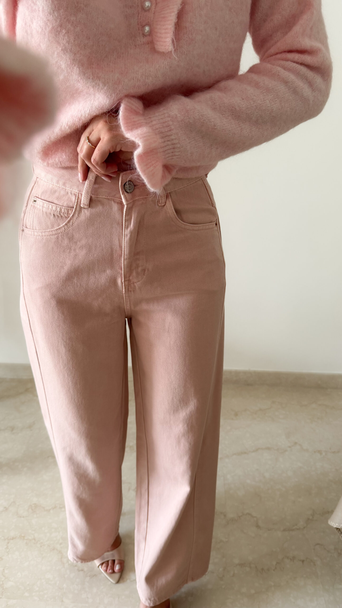 Pull rose doux à col volanté avec boutons perles porté avec un pantalon rose coupe droite.