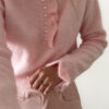 Pull rose doux à col volanté avec boutons perles porté avec un pantalon rose coupe droite.