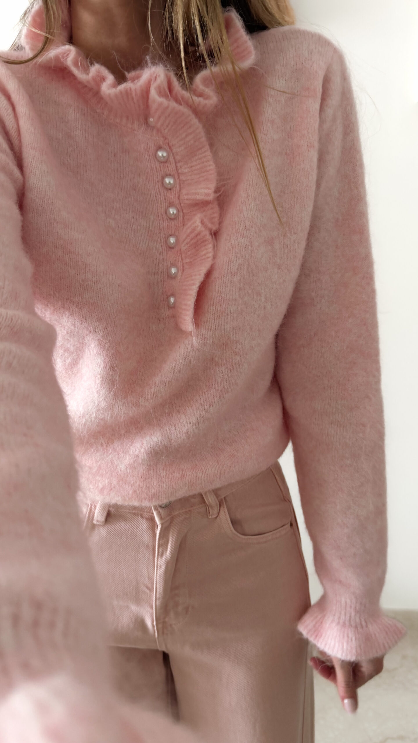 Pull rose doux à col volanté avec boutons perles porté avec un pantalon rose coupe droite.