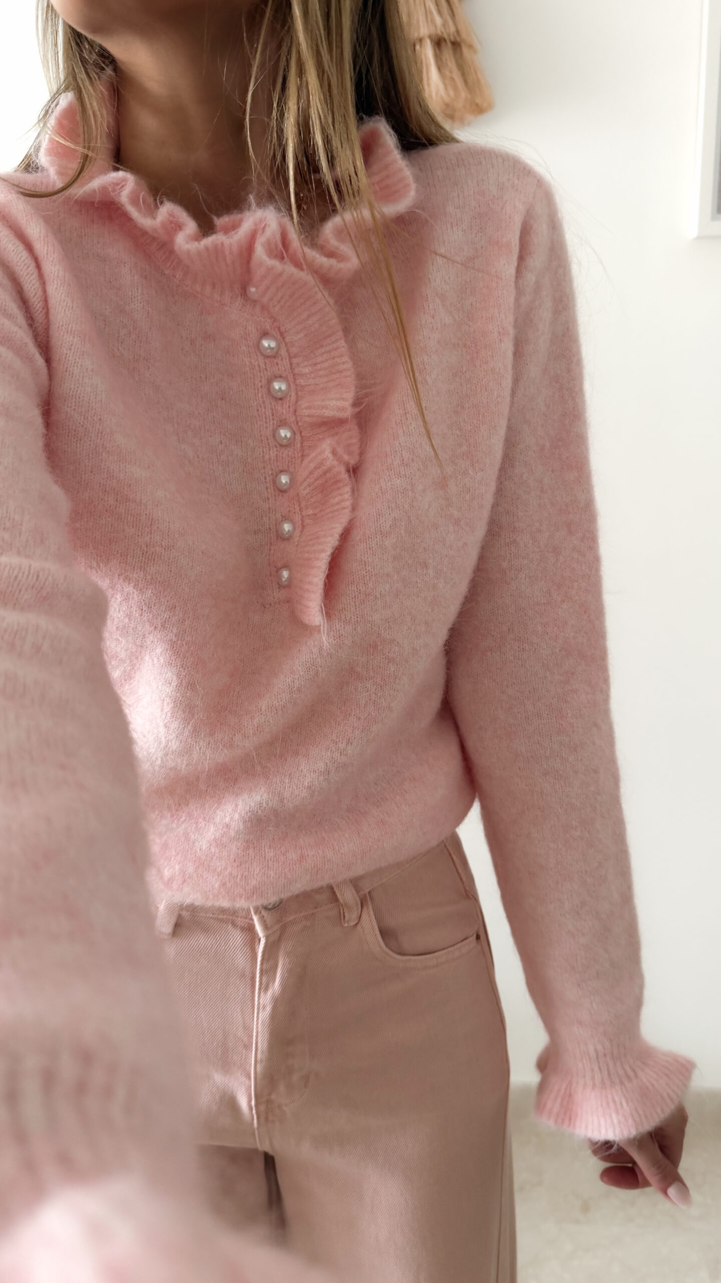 Pull rose doux à col volanté avec boutons perles porté avec un pantalon rose coupe droite.