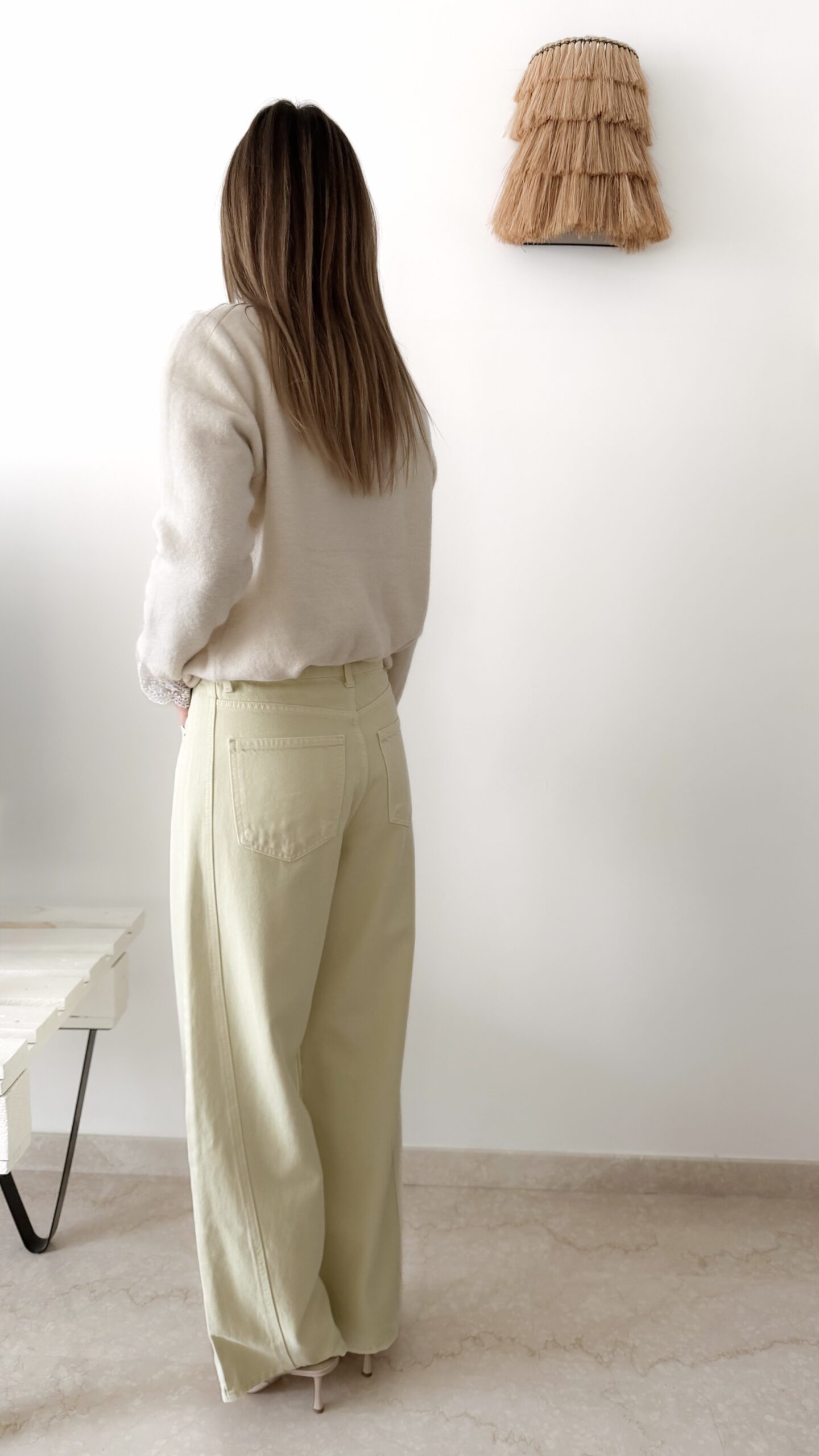 Femme portant un pull crème à détails dentelle aux poignets et un jean large jaune pâle, avec sandales beiges.