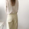 Femme portant un pull crème à détails dentelle aux poignets et un jean large jaune pâle, avec sandales beiges.