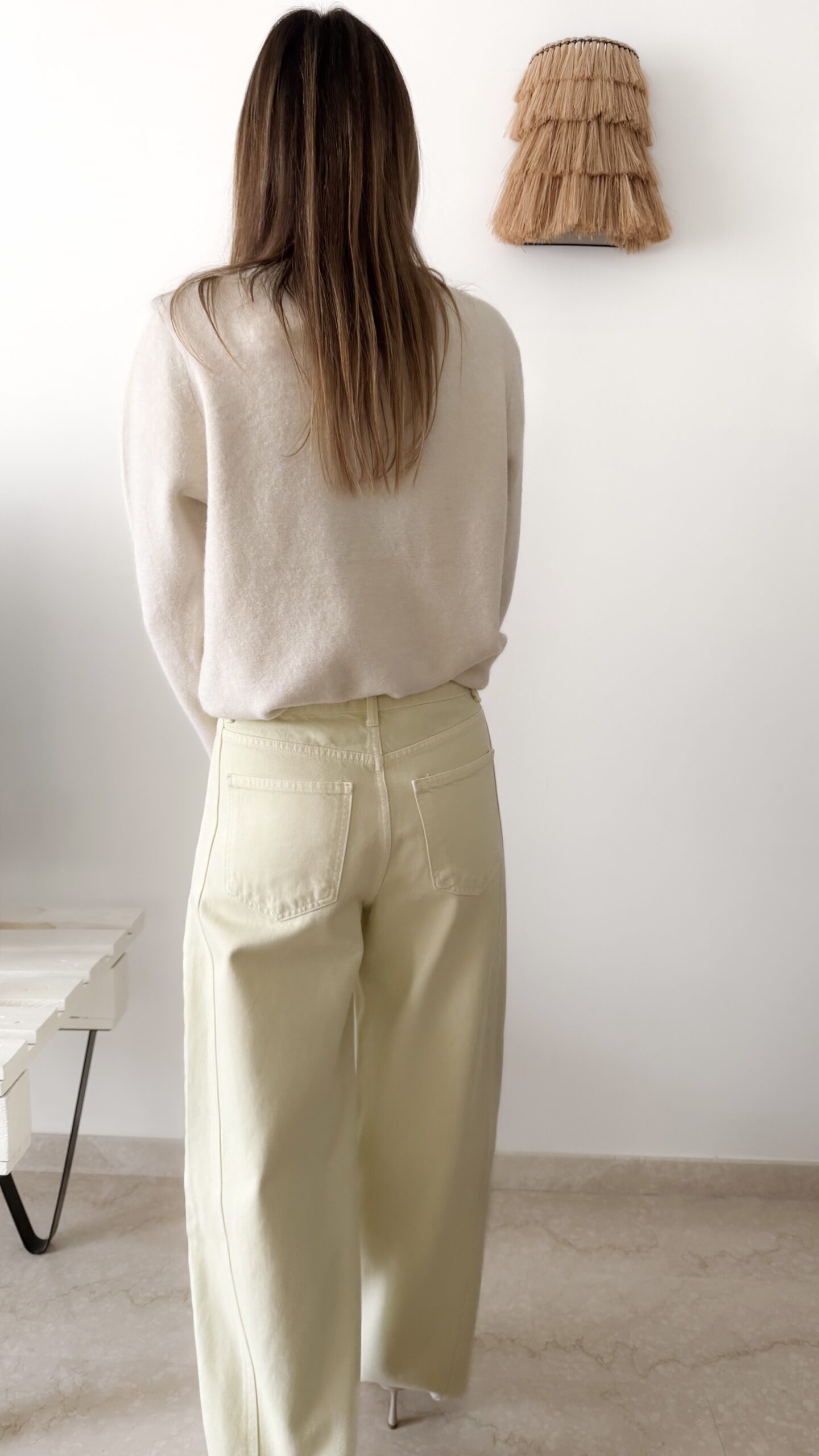 Femme portant un pull crème à détails dentelle aux poignets et un jean large jaune pâle, avec sandales beiges.