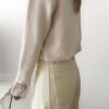 Femme portant un pull crème à détails dentelle aux poignets et un jean large jaune pâle, avec sandales beiges.