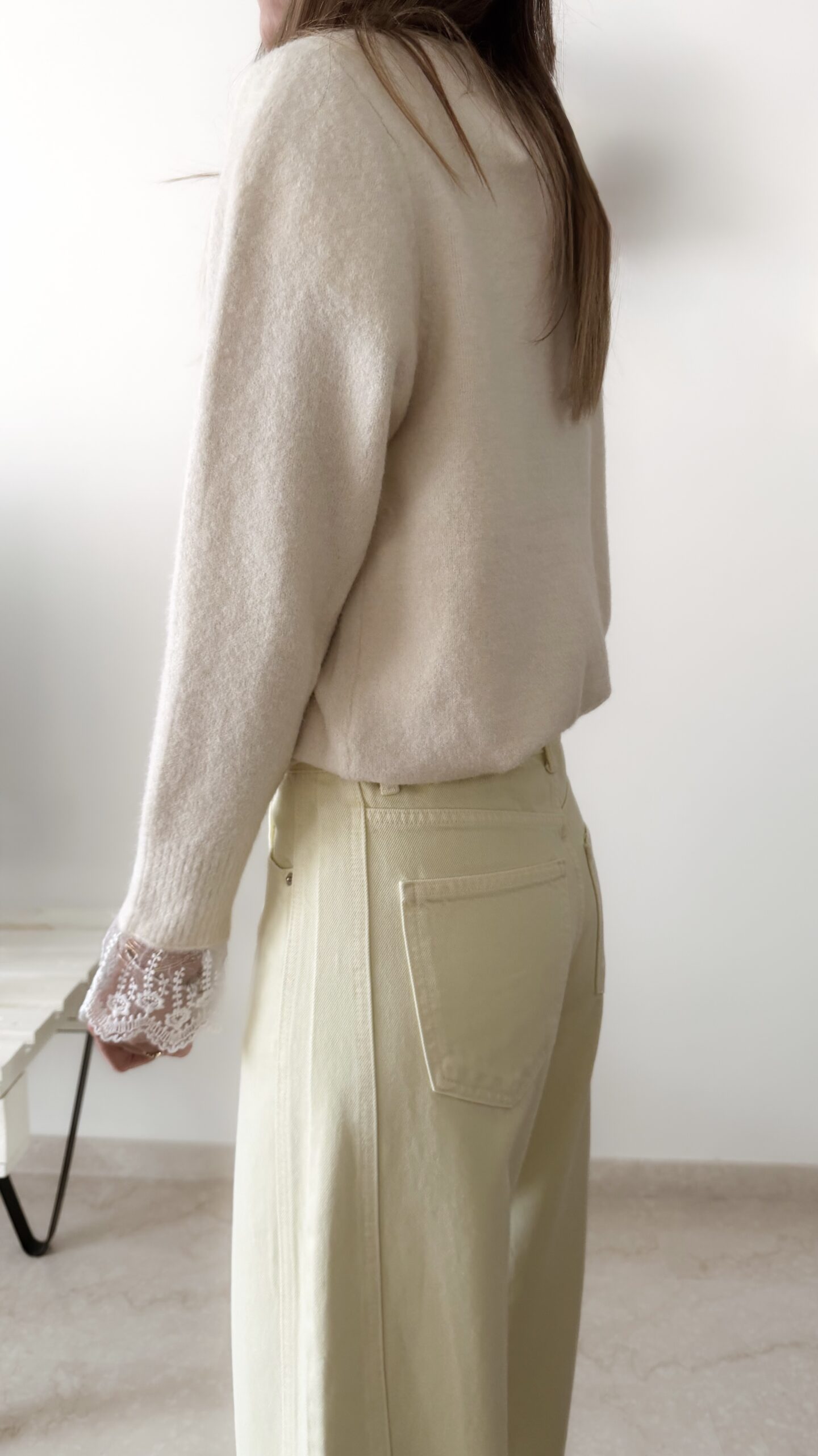 Femme portant un pull crème à détails dentelle aux poignets et un jean large jaune pâle, avec sandales beiges.