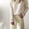 Femme portant un pull crème à détails dentelle aux poignets et un jean large jaune pâle, avec sandales beiges.
