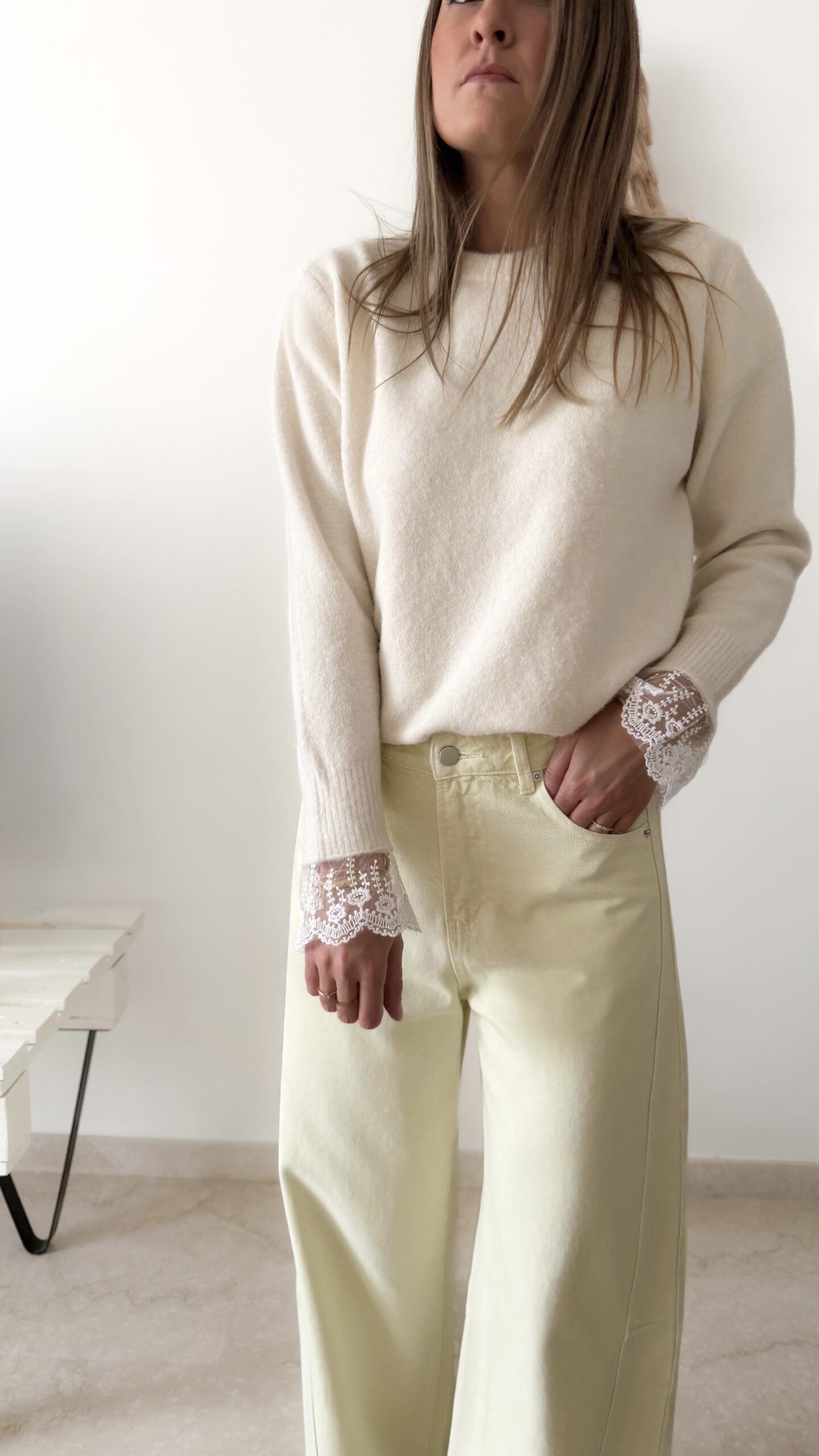 Femme portant un pull crème à détails dentelle aux poignets et un jean large jaune pâle, avec sandales beiges.