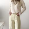 Femme portant un pull crème à détails dentelle aux poignets et un jean large jaune pâle, avec sandales beiges.
