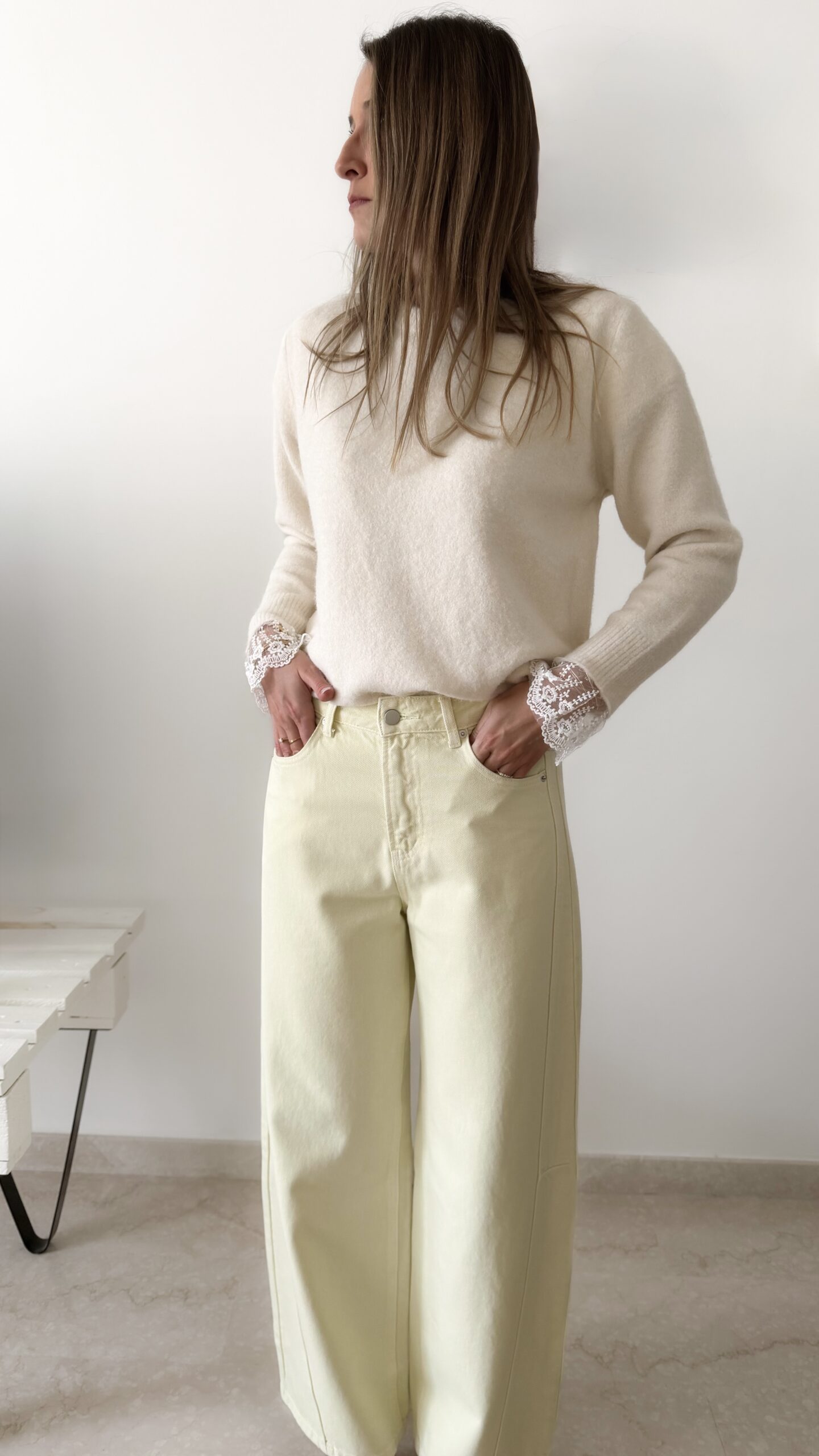 Femme portant un pull crème à détails dentelle aux poignets et un jean large jaune pâle, avec sandales beiges.