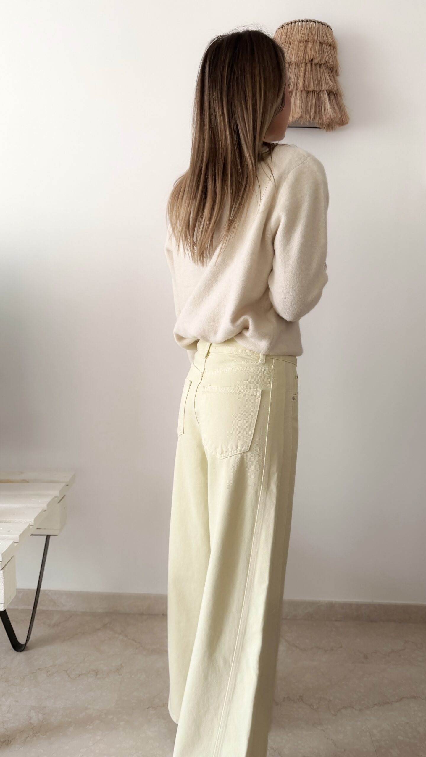 Femme portant un pull crème à détails dentelle aux poignets et un jean large jaune pâle, avec sandales beiges.