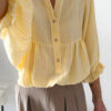 Blouse jaune à rayures blanches, coupe ample avec boutons et manches trois-quarts, portée avec un pantalon fluide beige.