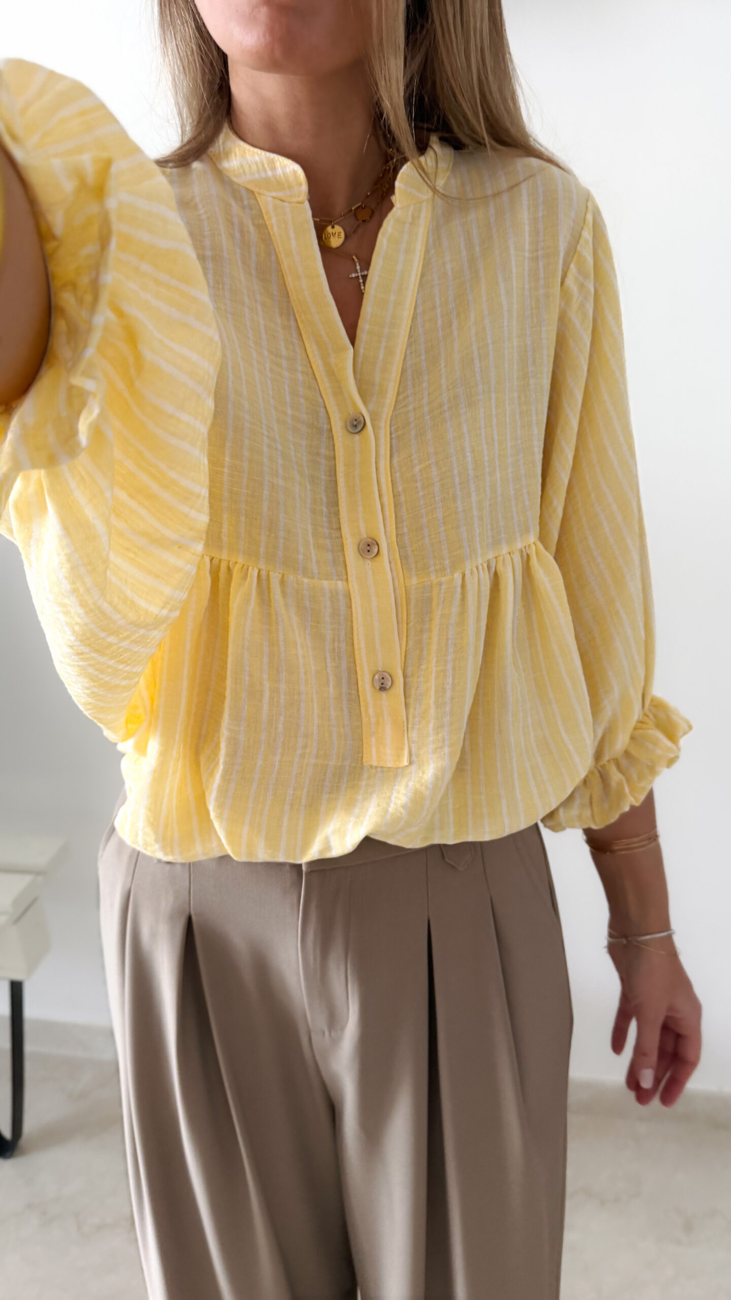 Blouse jaune à rayures blanches, coupe ample avec boutons et manches trois-quarts, portée avec un pantalon fluide beige.