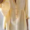 Blouse jaune à rayures blanches, coupe ample avec boutons et manches trois-quarts, portée avec un pantalon fluide beige.