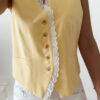 Gilet sans manches à boutons avec finition dentelle, une pièce élégante et féminine disponible en rose et jaune.