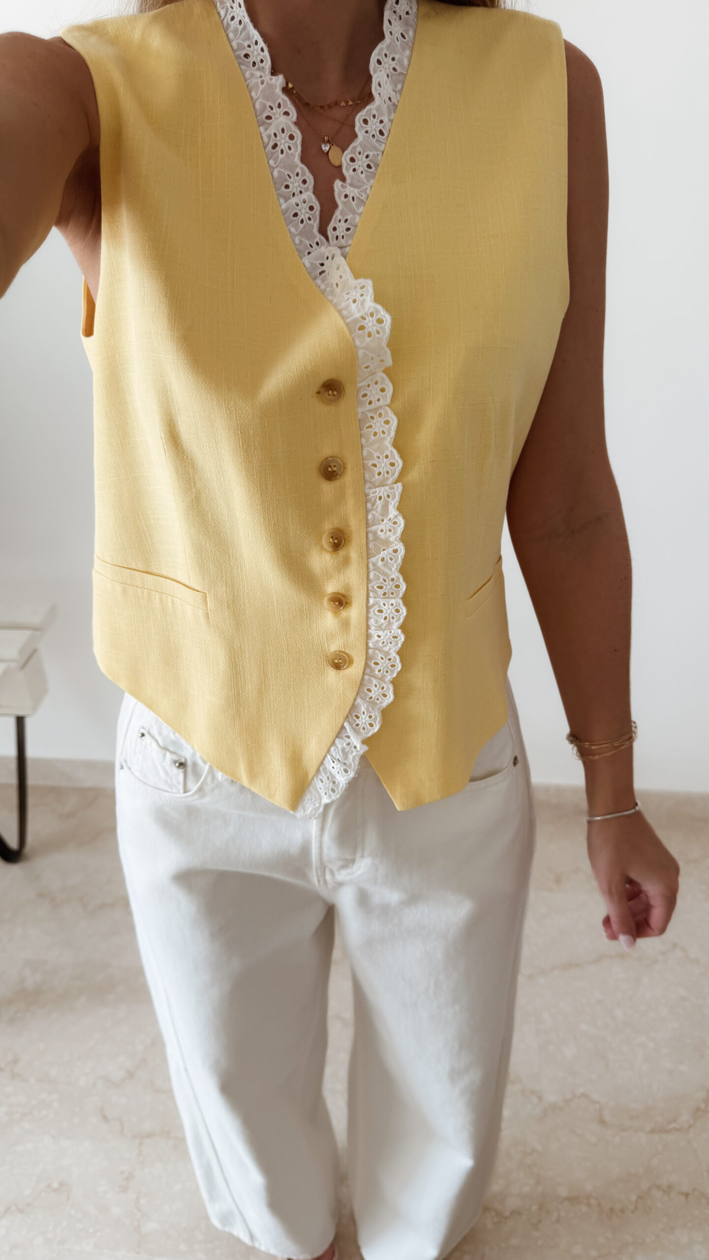 Gilet sans manches à boutons avec finition dentelle, une pièce élégante et féminine disponible en rose et jaune.
