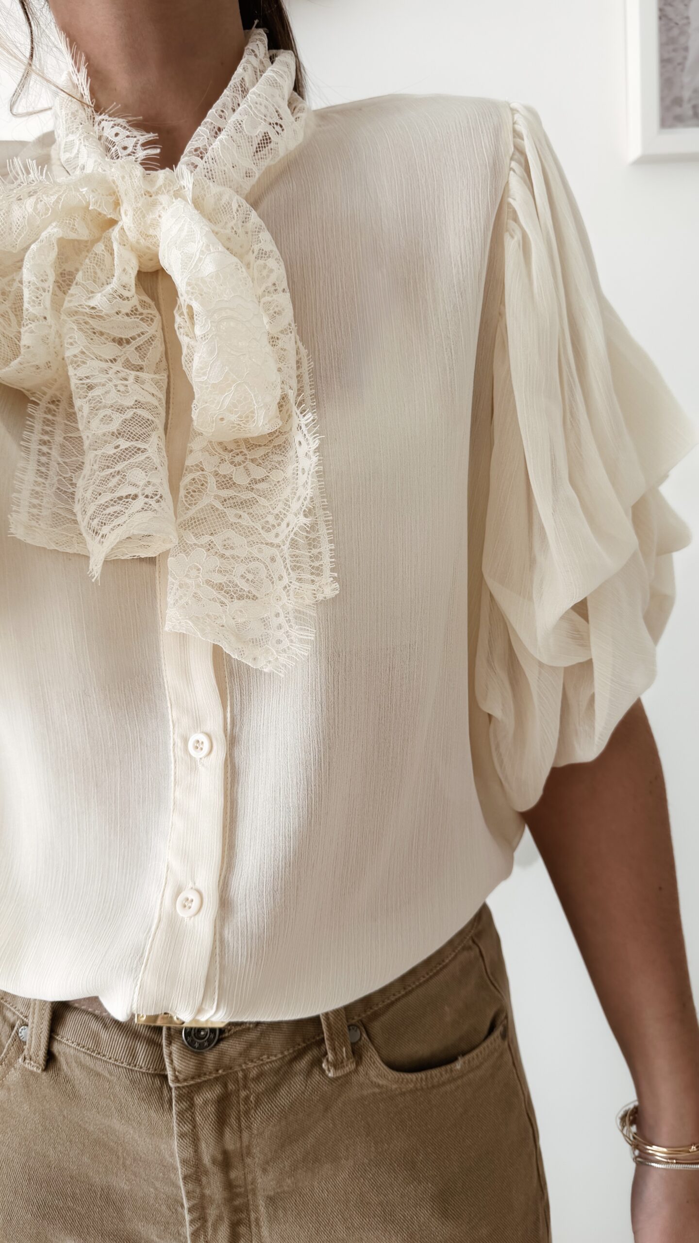 Blouse écrue avec col lavallière en dentelle et manches volantées, une pièce romantique et élégante.