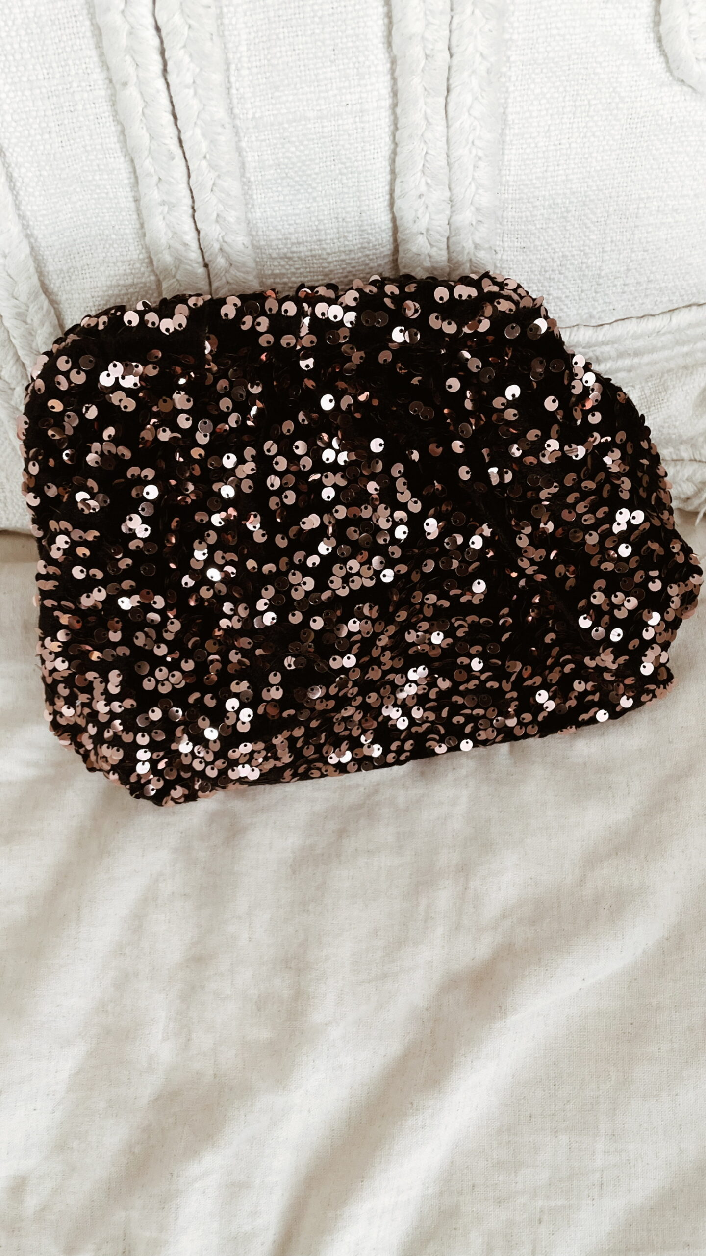 Femme tenant un sac à sequins chocolat scintillant, assorti à une tenue brune élégante avec chemisier et gilet en laine.