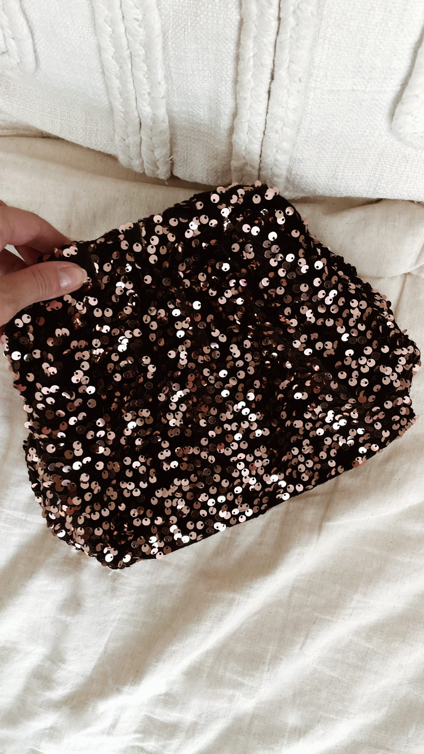 Femme tenant un sac à sequins chocolat scintillant, assorti à une tenue brune élégante avec chemisier et gilet en laine.