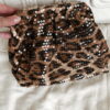 Femme tenant un sac à sequins léopard scintillant, assorti à une tenue brune élégante avec chemisier et blazer en laine.