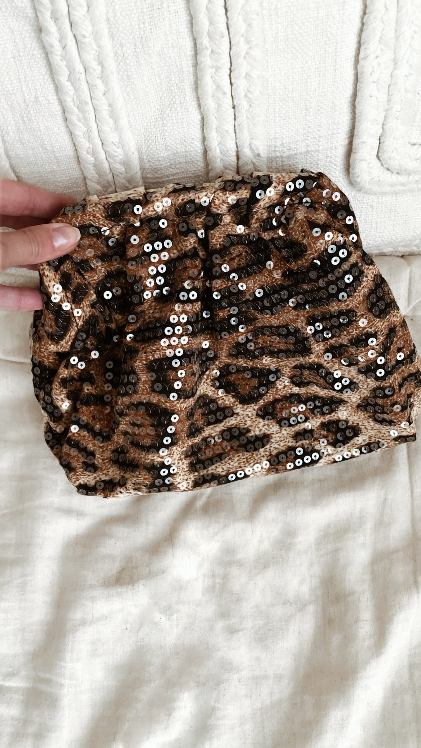 Femme tenant un sac à sequins léopard scintillant, assorti à une tenue brune élégante avec chemisier et blazer en laine.
