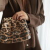 Femme tenant un sac à sequins léopard scintillant, assorti à une tenue brune élégante avec chemisier et blazer en laine.
